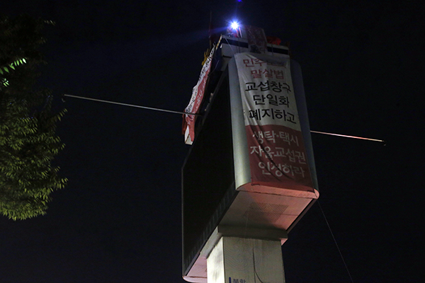 ▲ 부산시청 광고탑 위에서 8월 21일 현재 128일째 고공농성을 벌이고 있는 부산일반노조 부산합동양조(생탁) 현장위원회 송복남 총무부장과 공공운수노조 택시지부 부산지회 심정보 조합원이 결의대회 참가자들을 향해 불빛을 흔들어 보이고 있다.